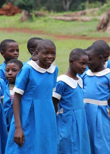 This photo shows a group of girls and boys in Cameroon wearing blue and white school uniforms, walking together and smiling.