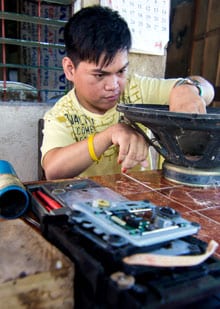 This photo shows a young man in the Philippines sitting at a table and fixing some sound equipment.