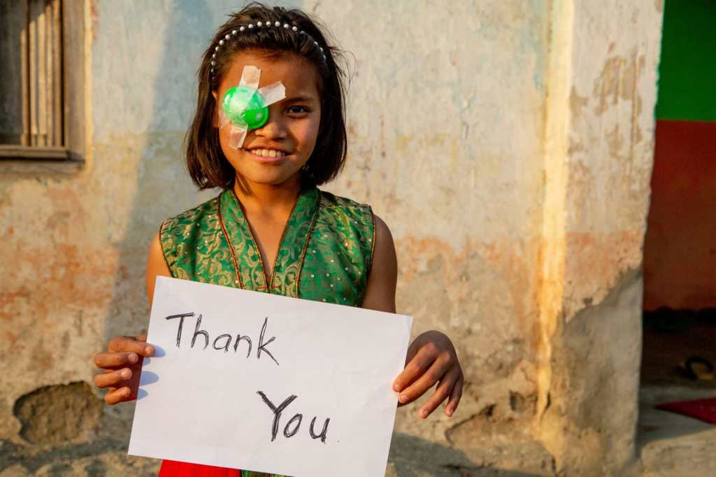 Reena smiling at the camera holding a sign that says thank you.