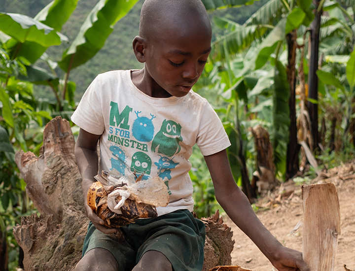Keneth sitting alone using banana leaves to make a ball.