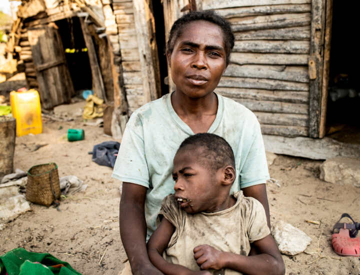 Maharavo being held by his mother as they sit outdoors in Madagascar.