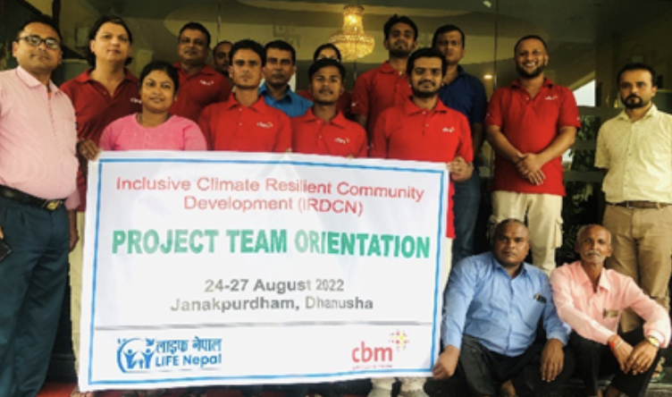 The CBM Nepal team standing and smiling behind a banner on climate resilience.