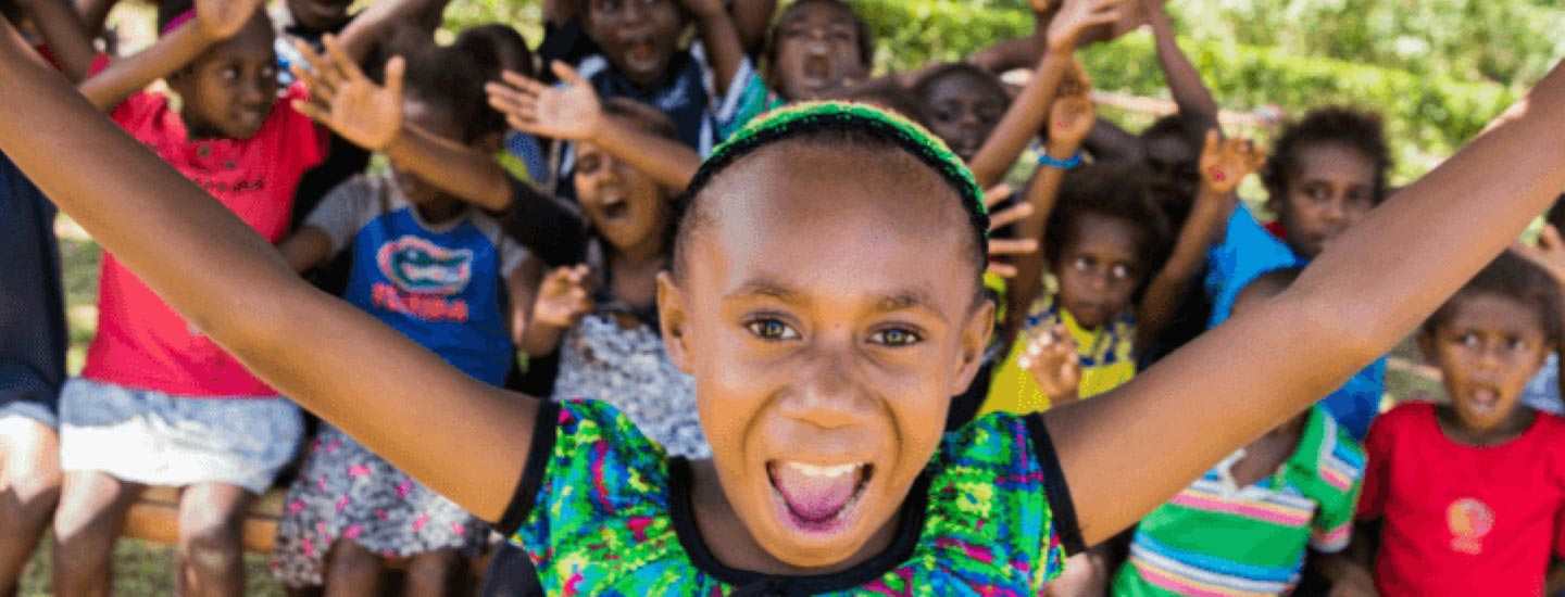 Smiling girl with outstretched arms with a group of children in the background