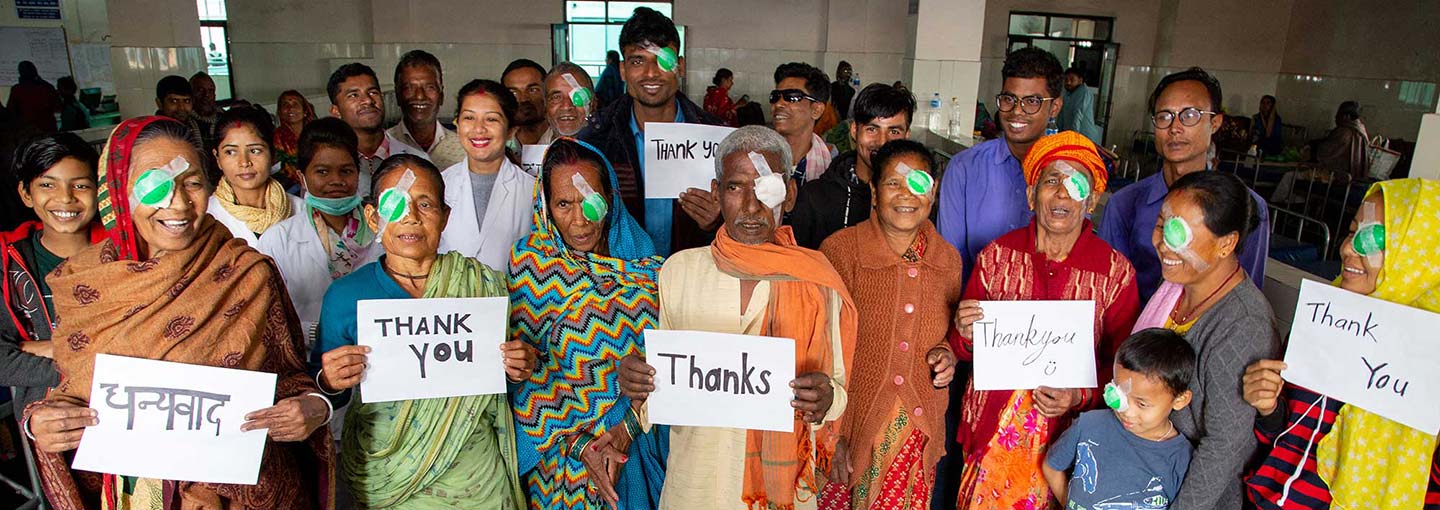 Group of people in Nepal each wearing an eye patch and holding signs saying thank you