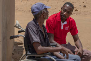 CBM Zimbabwe Emergency Response Team member Allen Chaitezvi with Ezekiel Rukuruva, 62, in his new wheelchair at his home in a food-insecure area of Chiredzi, Zimbabwe