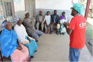 A CBM worker speaking to a seated group of people in Kenya.