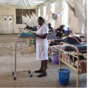 A nurse wearing a white uniform standing in a hospital ward in Nigeria.