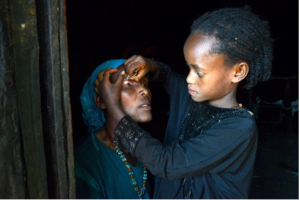 A young girl inspecting the eye of an older woman in Kenya.