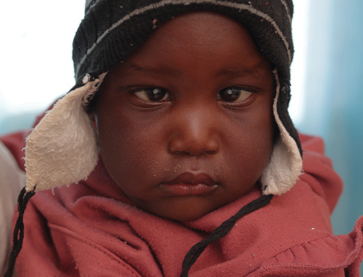 A girl in a pink jacket and black and white beanie staring at the camera