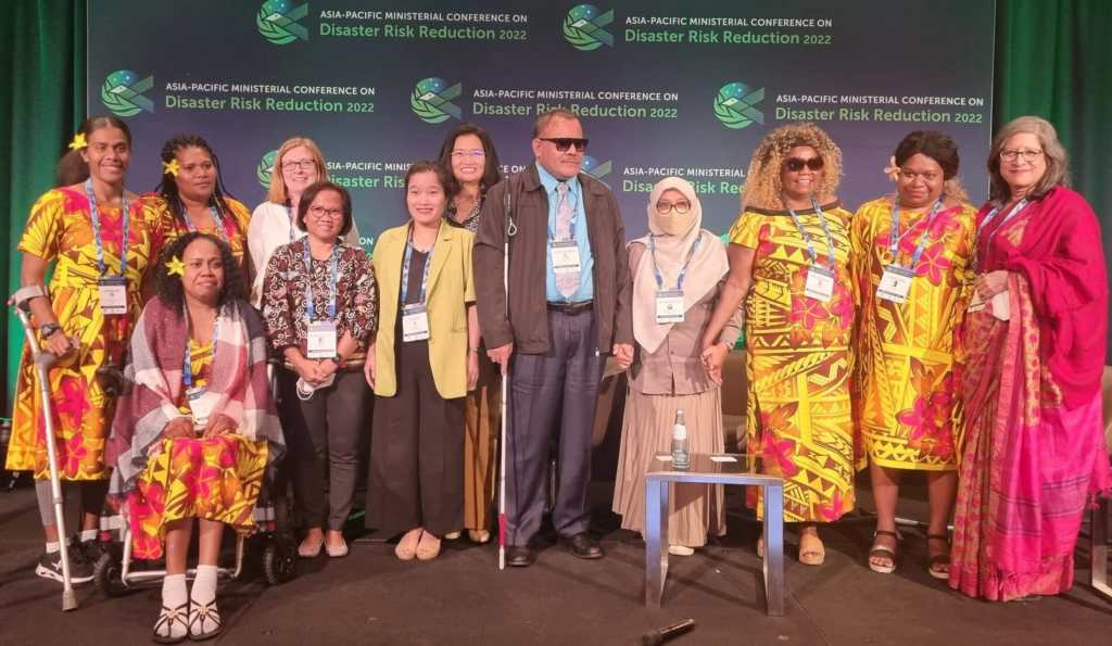 12 representatives of organisations of people with disabilities gather alongside each other on the stage of the Asia Pacific Ministerial Conference on Disaster Risk Reduction