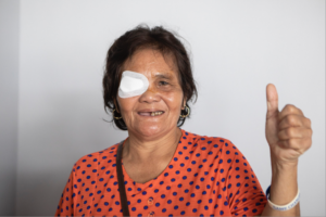 an elderly woman with an eye patch on her right eye with a thumbs up