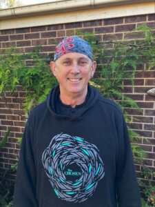 A male standing in front of a brick wall with a bandana on his head