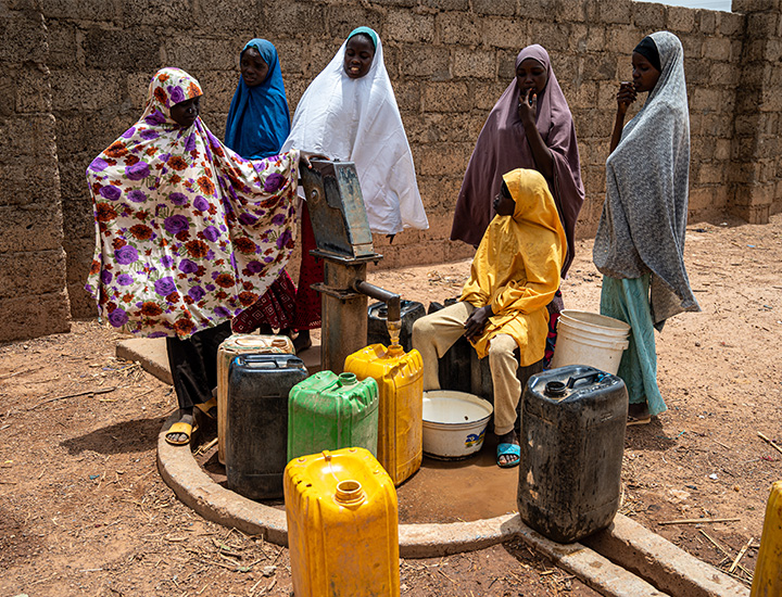 A group of women standing around containers used to carry water