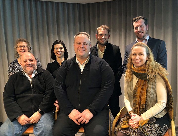 A group of people standing next to one another in a room. There are four men and three women.