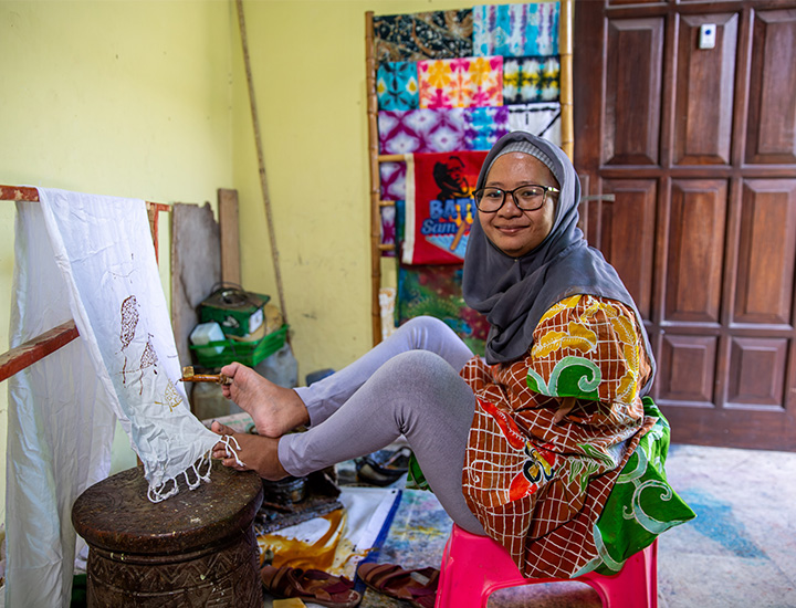 A woman with glasses in a red and yellow dress painting an artwork using her feet.