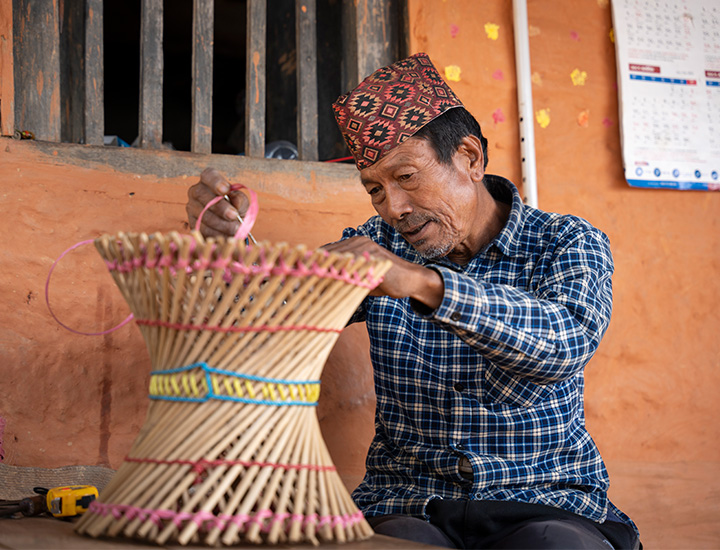 A man in a colourful fez focuses on weaving together a bamboo stool.