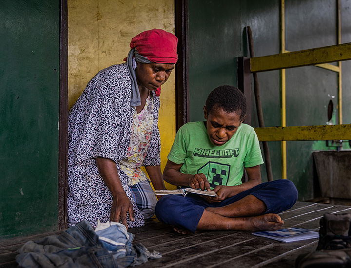 A boy trying to write while his mother looks over him