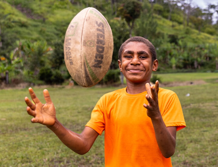 Smiling boy standing outside tossing a rugby ball.