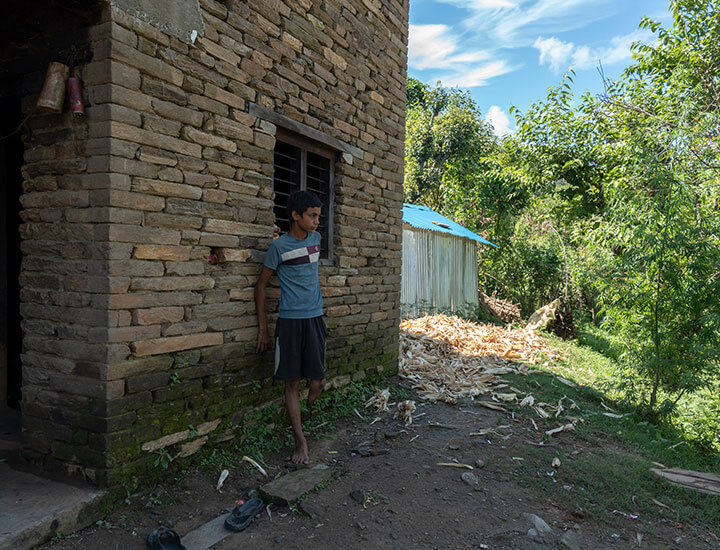 Boy with one leg leaning on brick house
