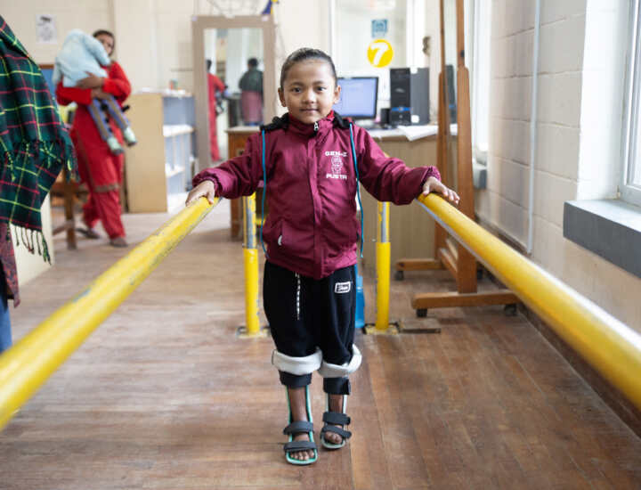 A little girl walking with her hands on the poles and walking devices